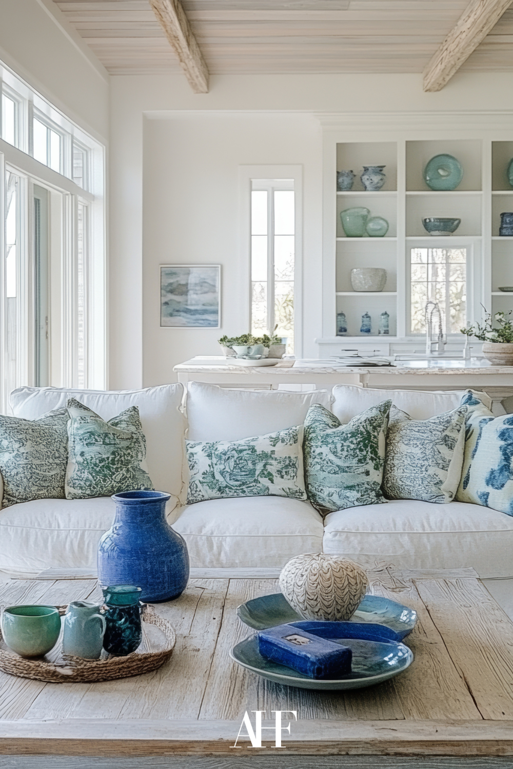 A closeup on a rustic wooden coffee table, a white sofa with coastal pillows. In the background, shelves with kitchen accessories. coastal design living room.