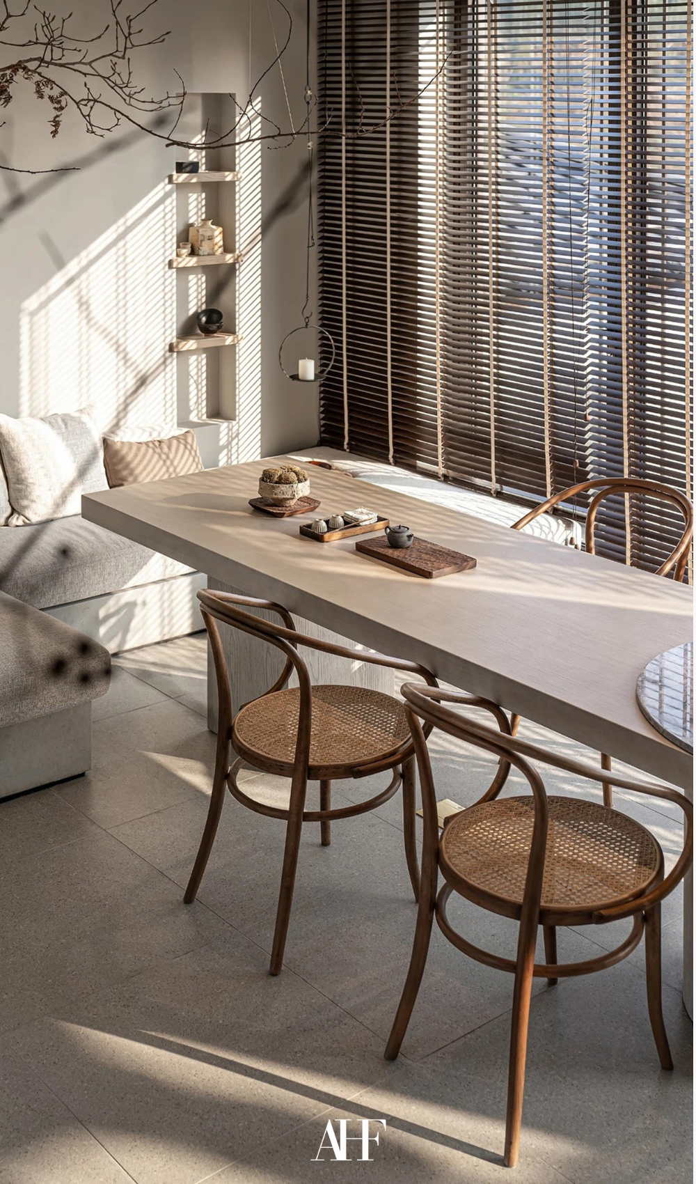 A japandi dining room with a large table and some chairs. A beige sofa and large windows. Wooden decor details.
