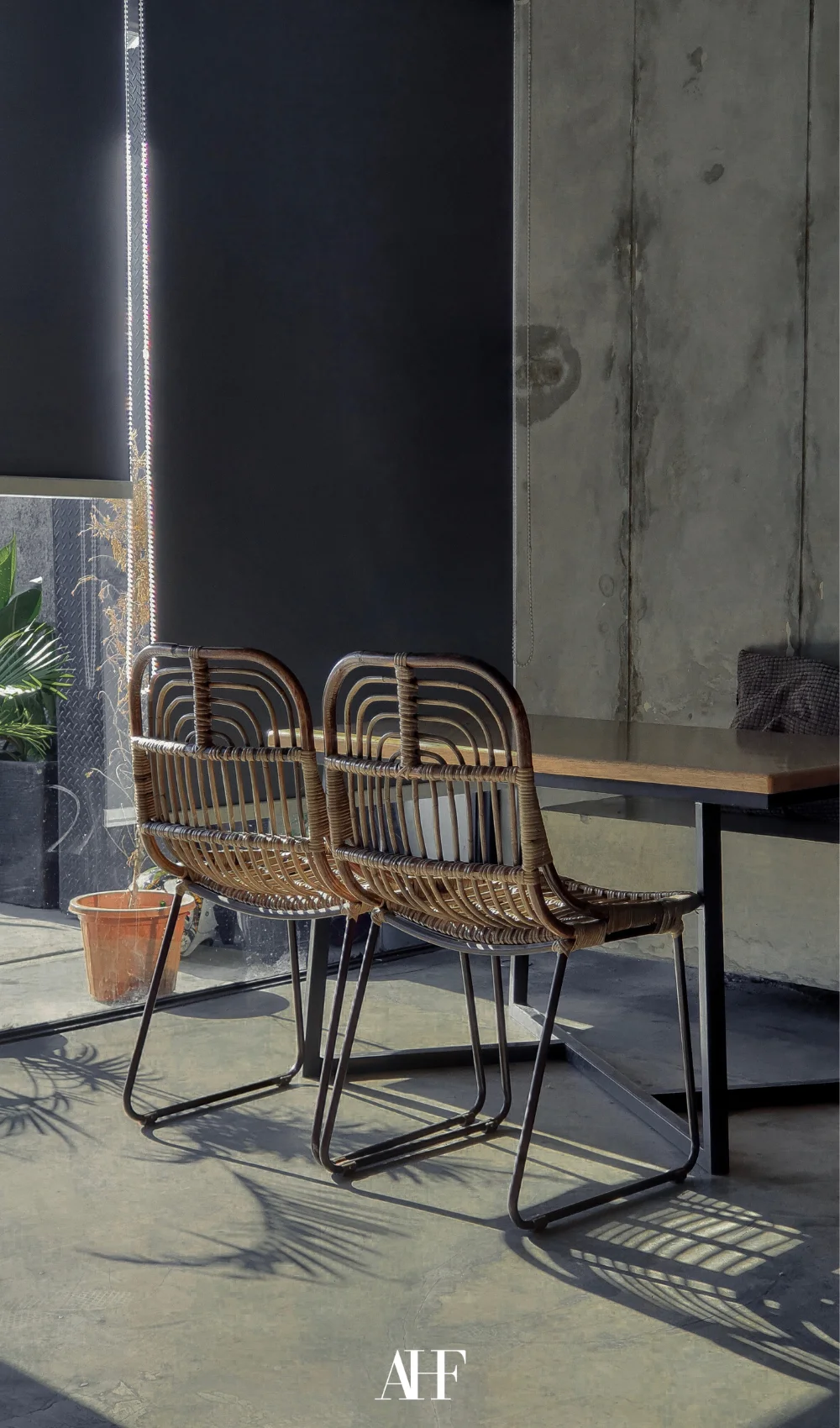 A industrial interior design home with concrete walls, wooden table and rattan chairs. Large windows.