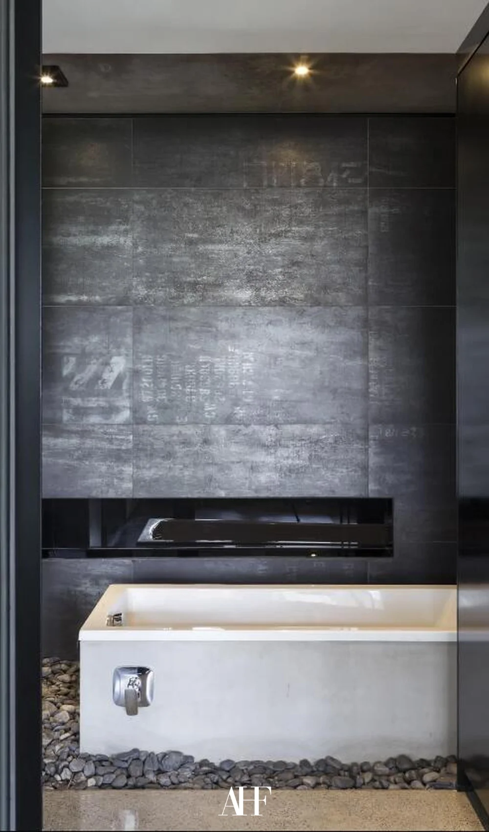 A black tile wall with a white bathtub in front of it. Industrial interior design.