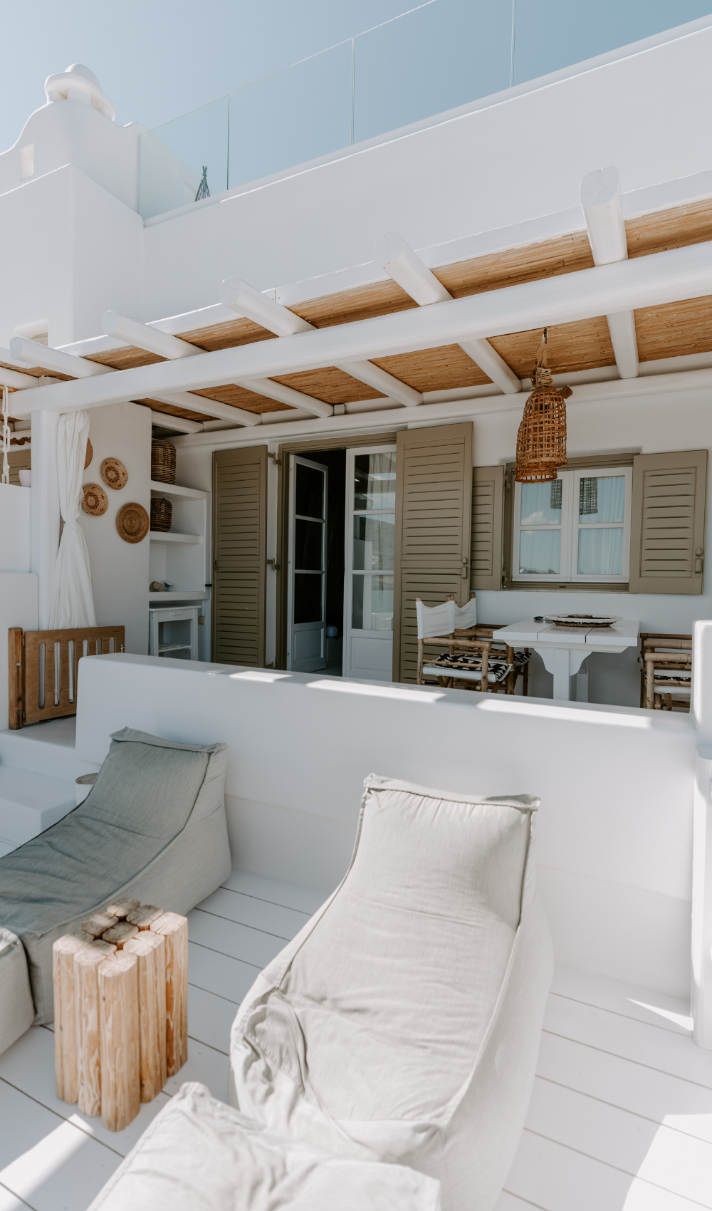 a beuatiful light and wooden summer patio with large pillows and furniture pieces.