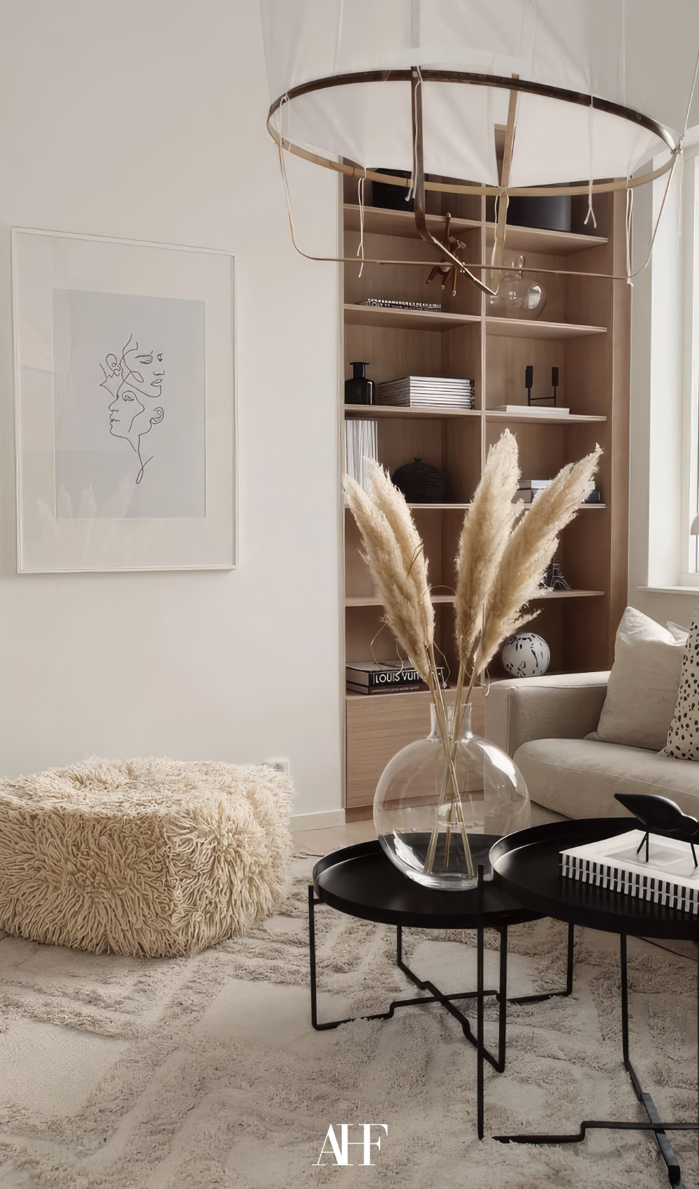 A coz living room with a perfect rug, a black coffee table, a wooden bookshelf and a beige sofa.
