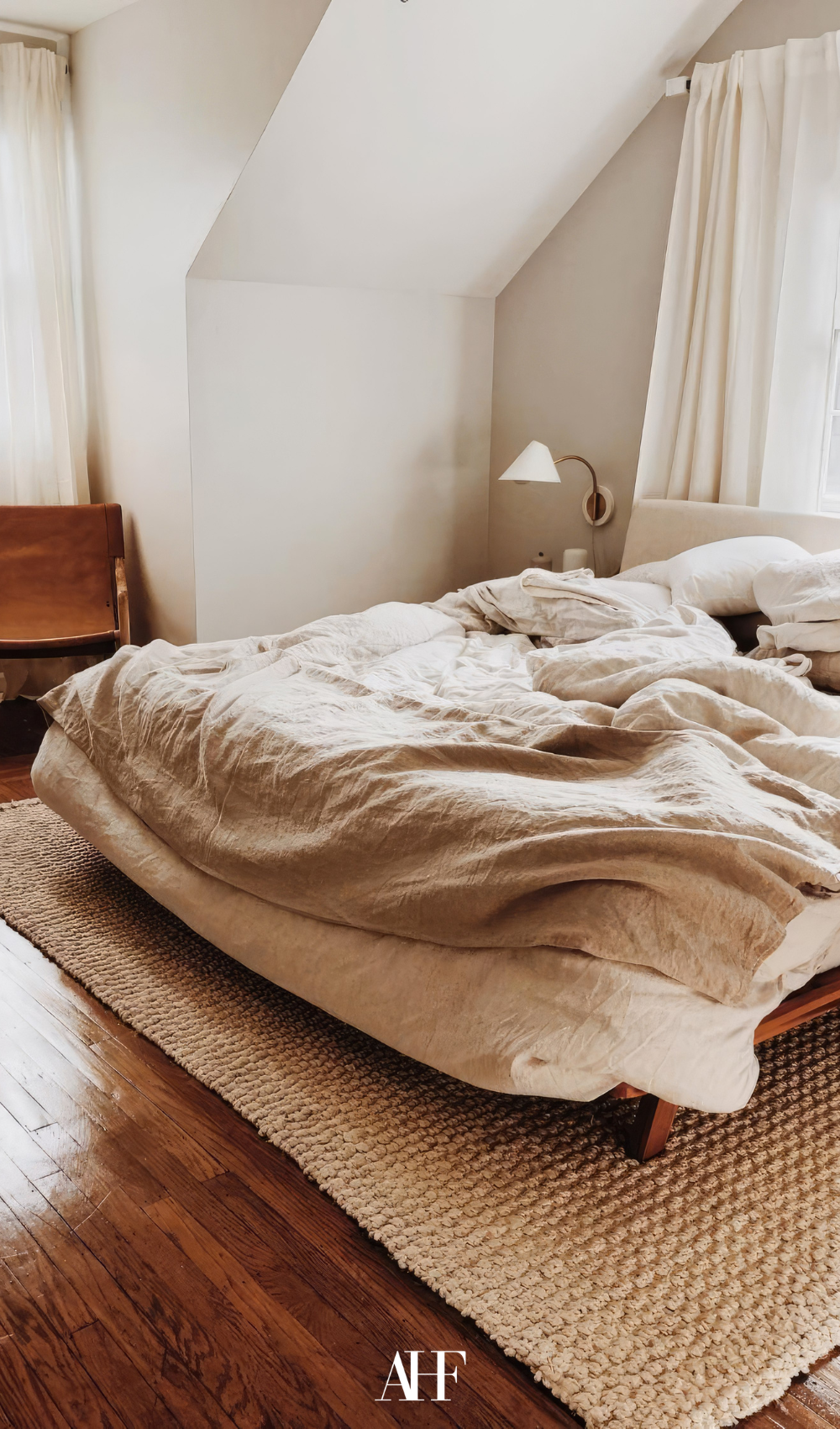 A bed with beige bedding, a jute rug under the bed, a wooden drawer in the corner. 