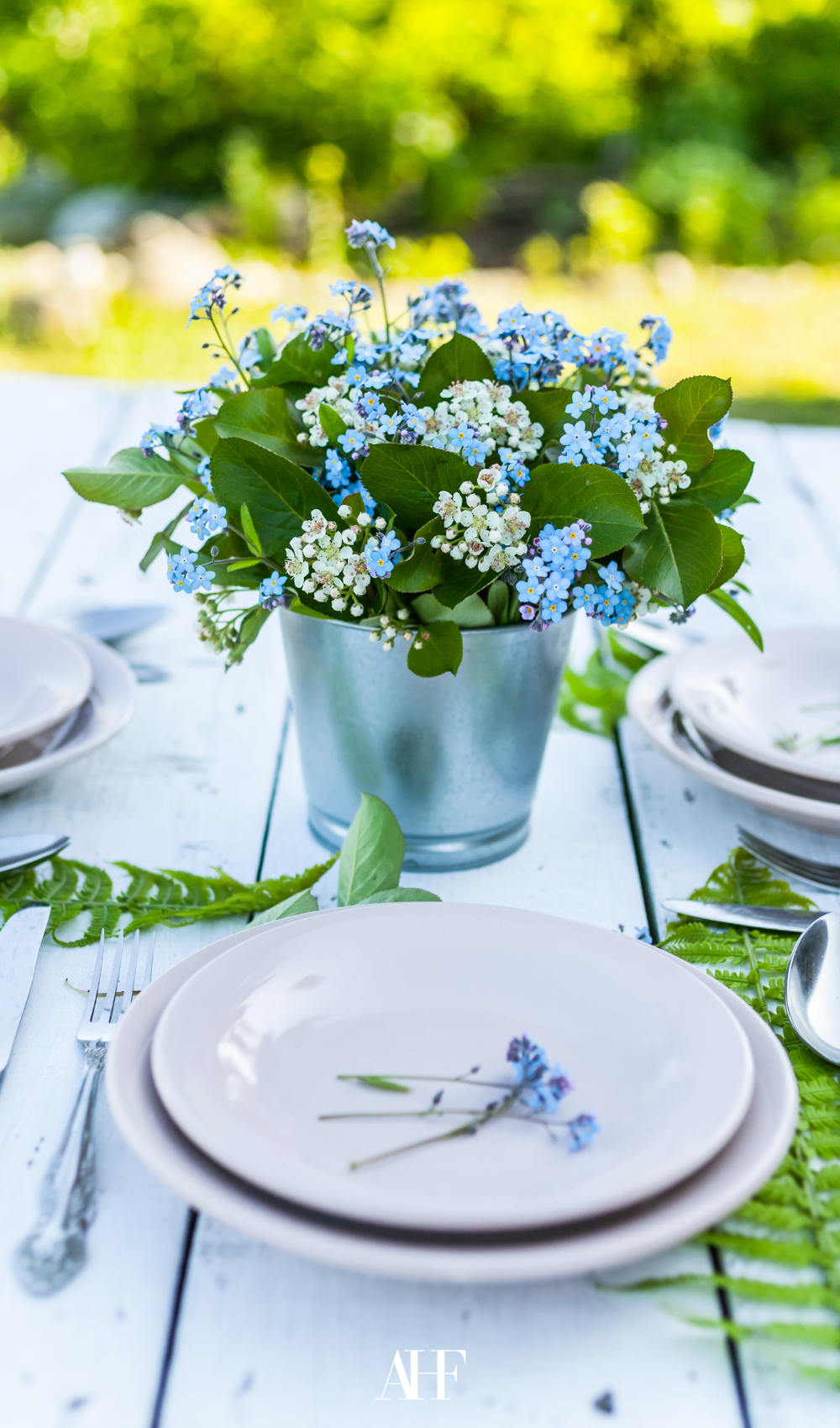 a summer table setting with a white wooden table, white dinnerware and a big blue floral on the table.