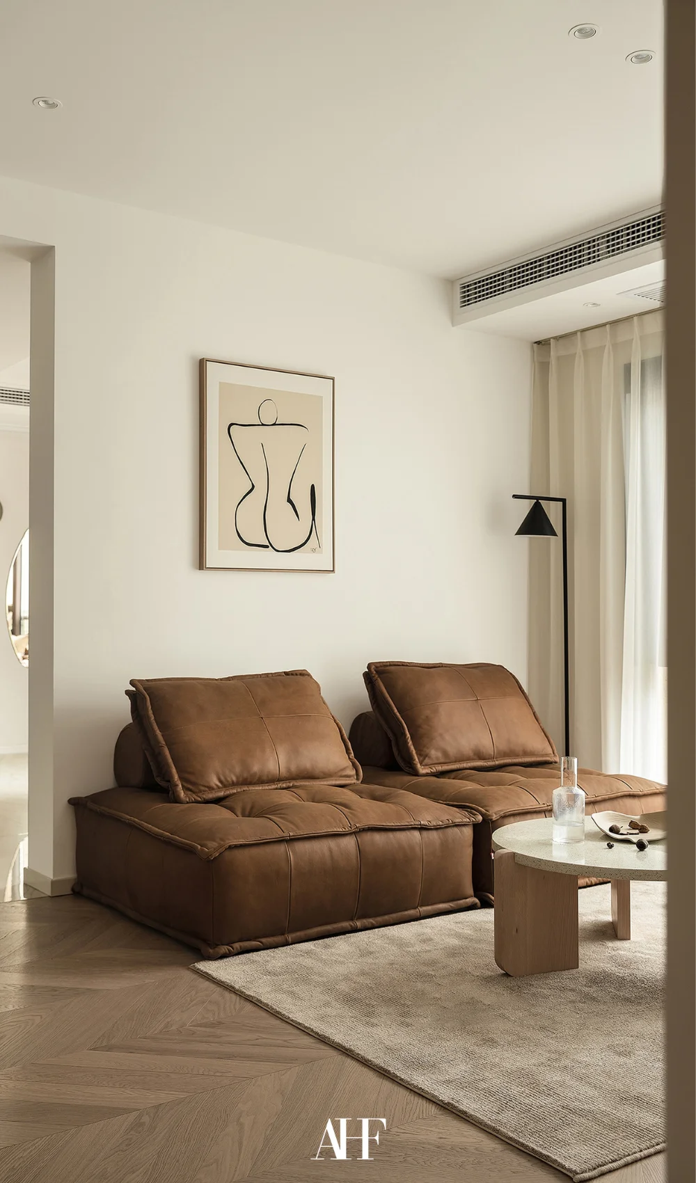 A small apartment living room with a brown leather couch, a wooden coffee table and a wall art above the couch. A rug.