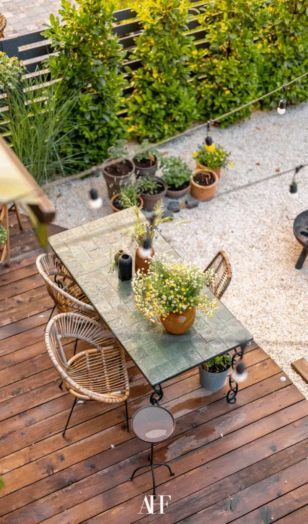 A beautiful patio taken from above on a dining table on a wooden deck. Wooden chairs and lots of greenery.