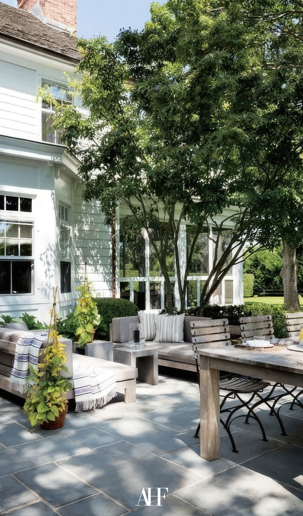 A beautiful summer patio with a lounge group and a wooden dining table. a large tree.