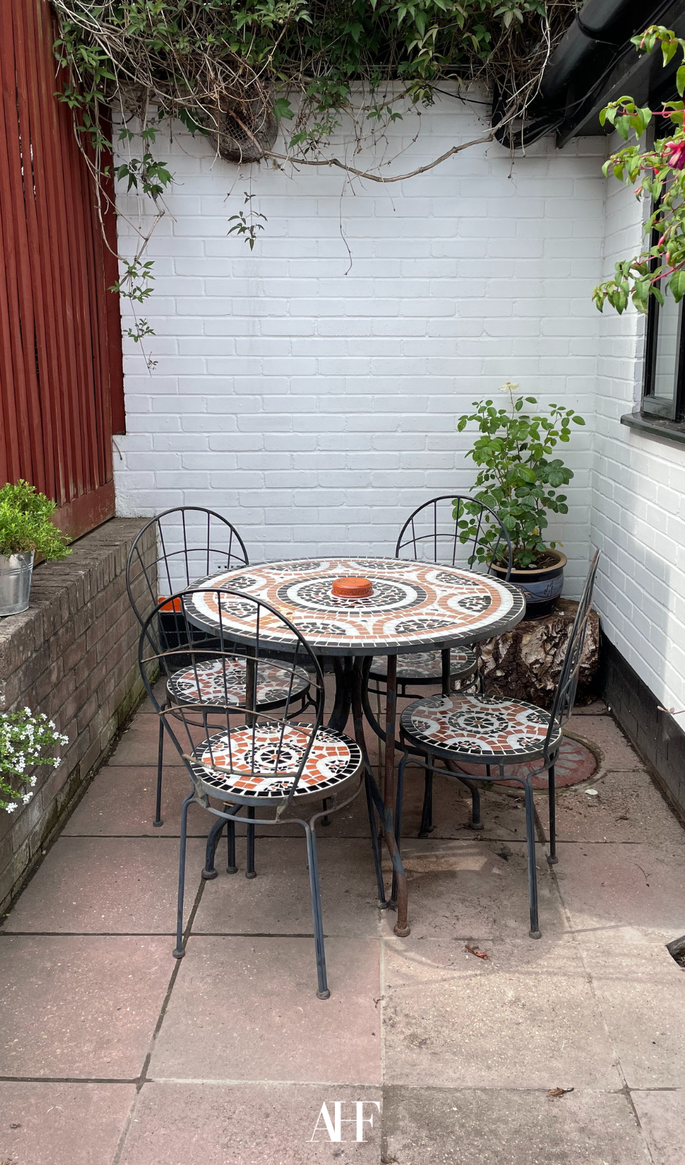 A cozy small patio with a boho table and boho chairs, beautiful patterns. A few plants.