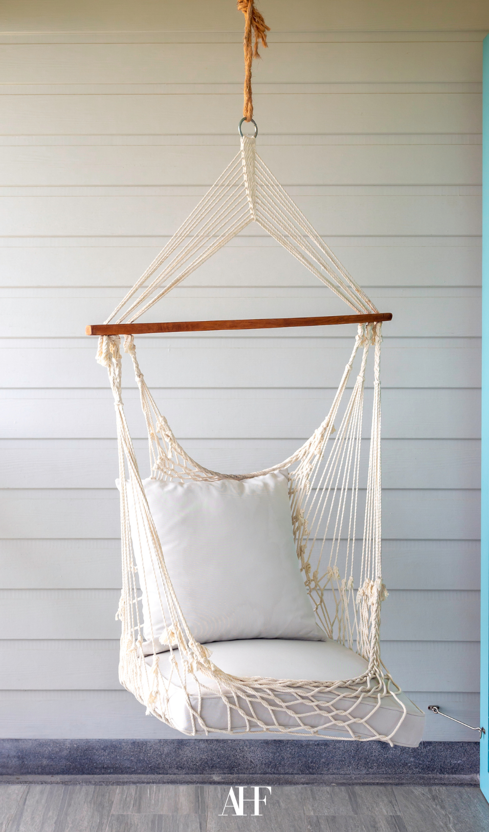 Hanging Hammock Chair in a sunroom. A white wooden wall behind it. A white pillow in it.