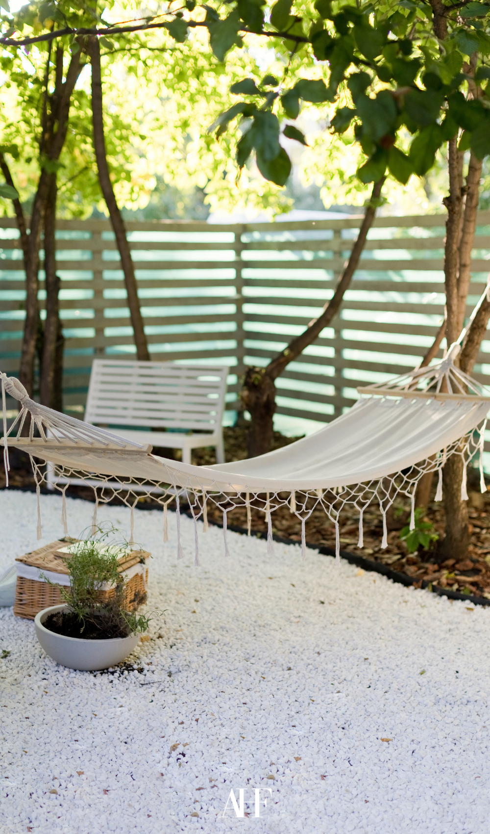 A hammock on a patio with white rocks as floor and a wooden fence.