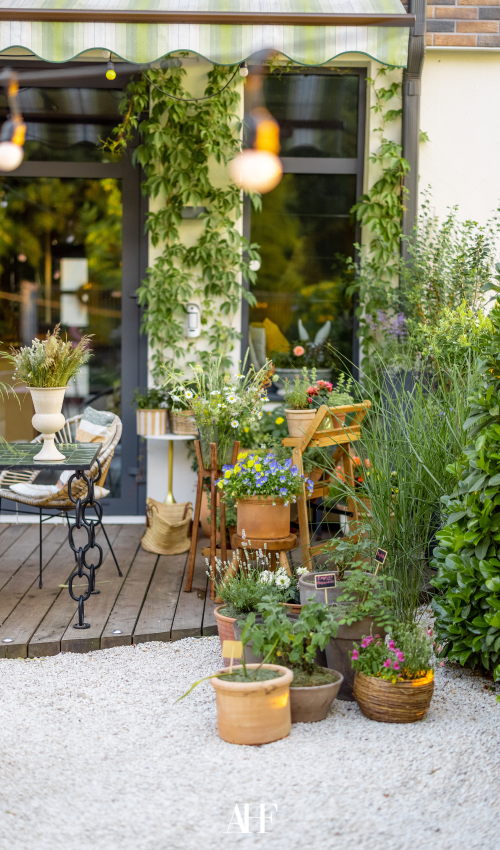 A beautiful small summer patio with lots of greenery and a table and two chairs.