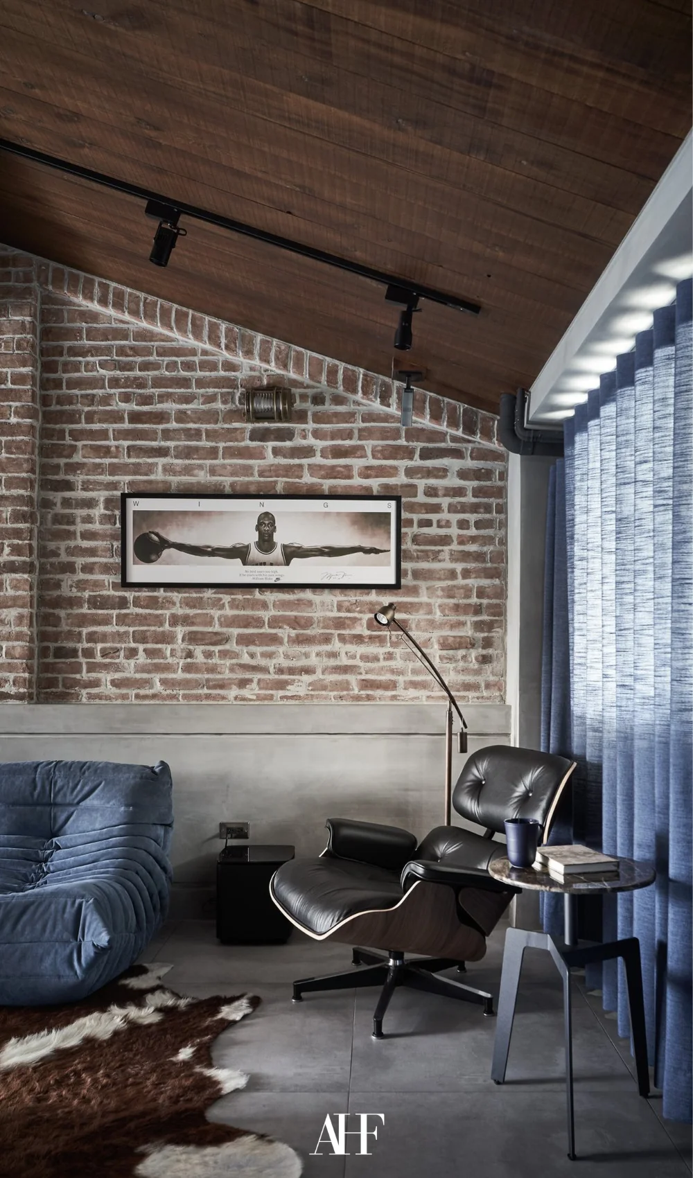 An industrial chic living room with a navy sofa, navy curtains, brick walls and a black eames chair.