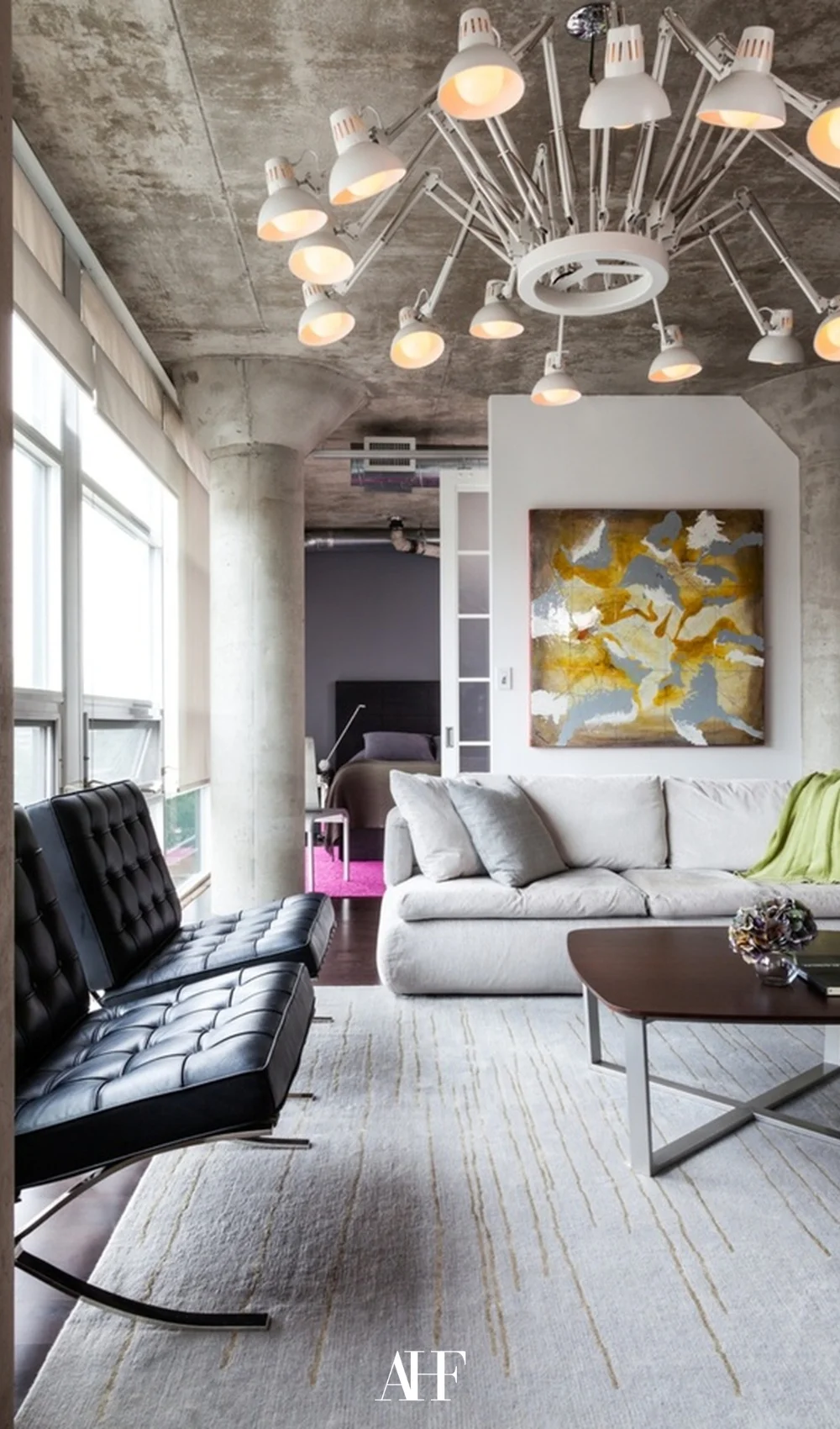 A industrial interior home with bold pops of colors, a grey sofa, two black armchairs and a wooden coffee table.