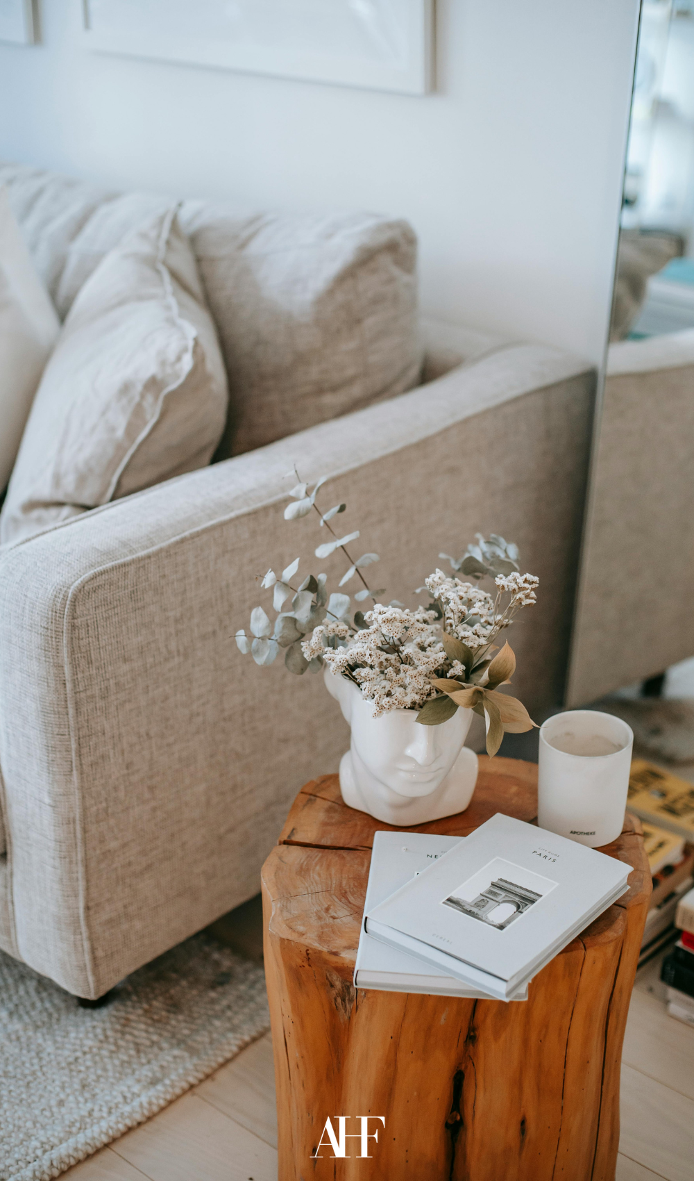 A beige linen sofa with a wooden coffee table with a plant, a candle and a book on it.