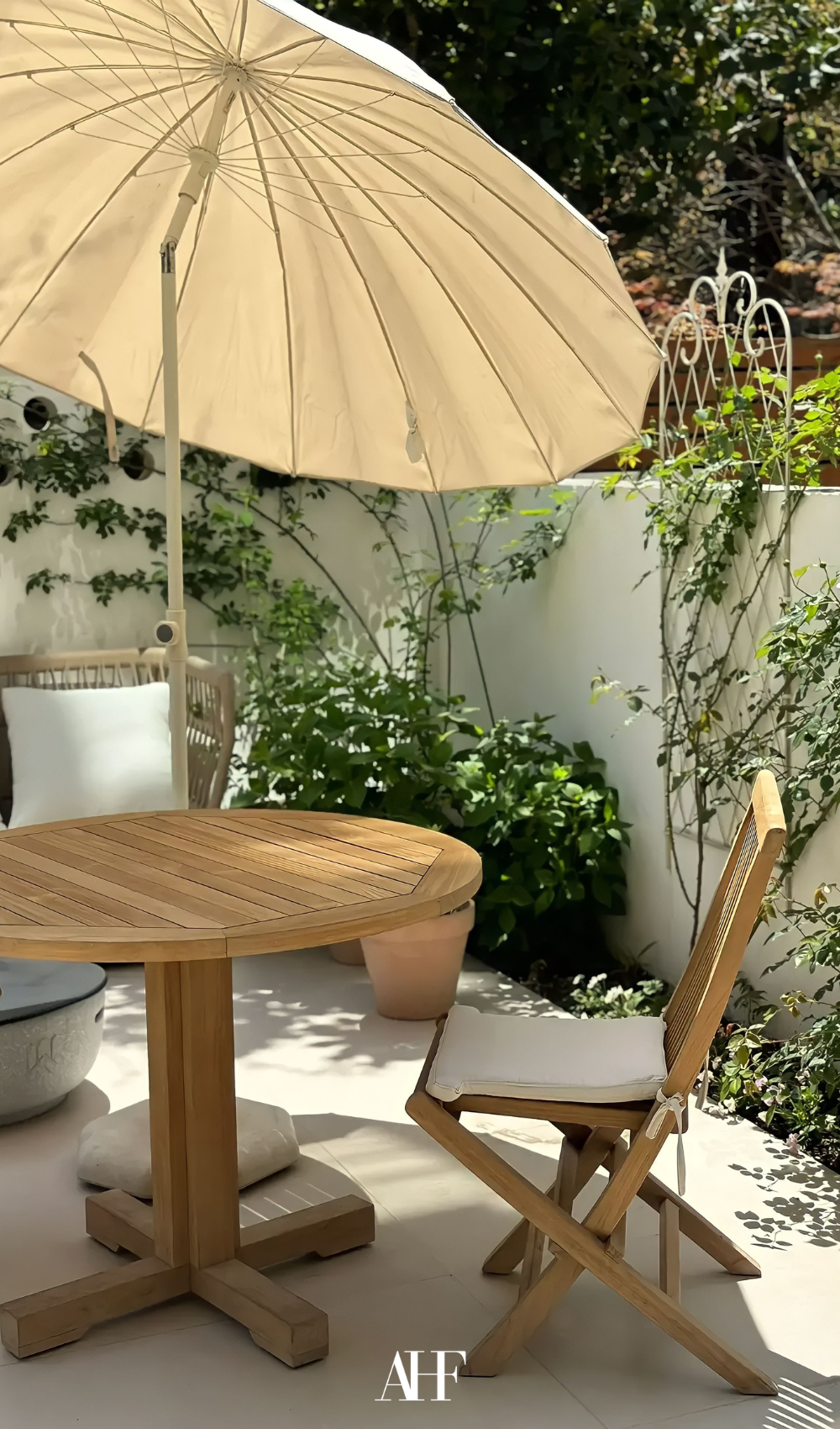 A very beautiful small summer patio with wooden furniture, a parasol and lots of greenery.