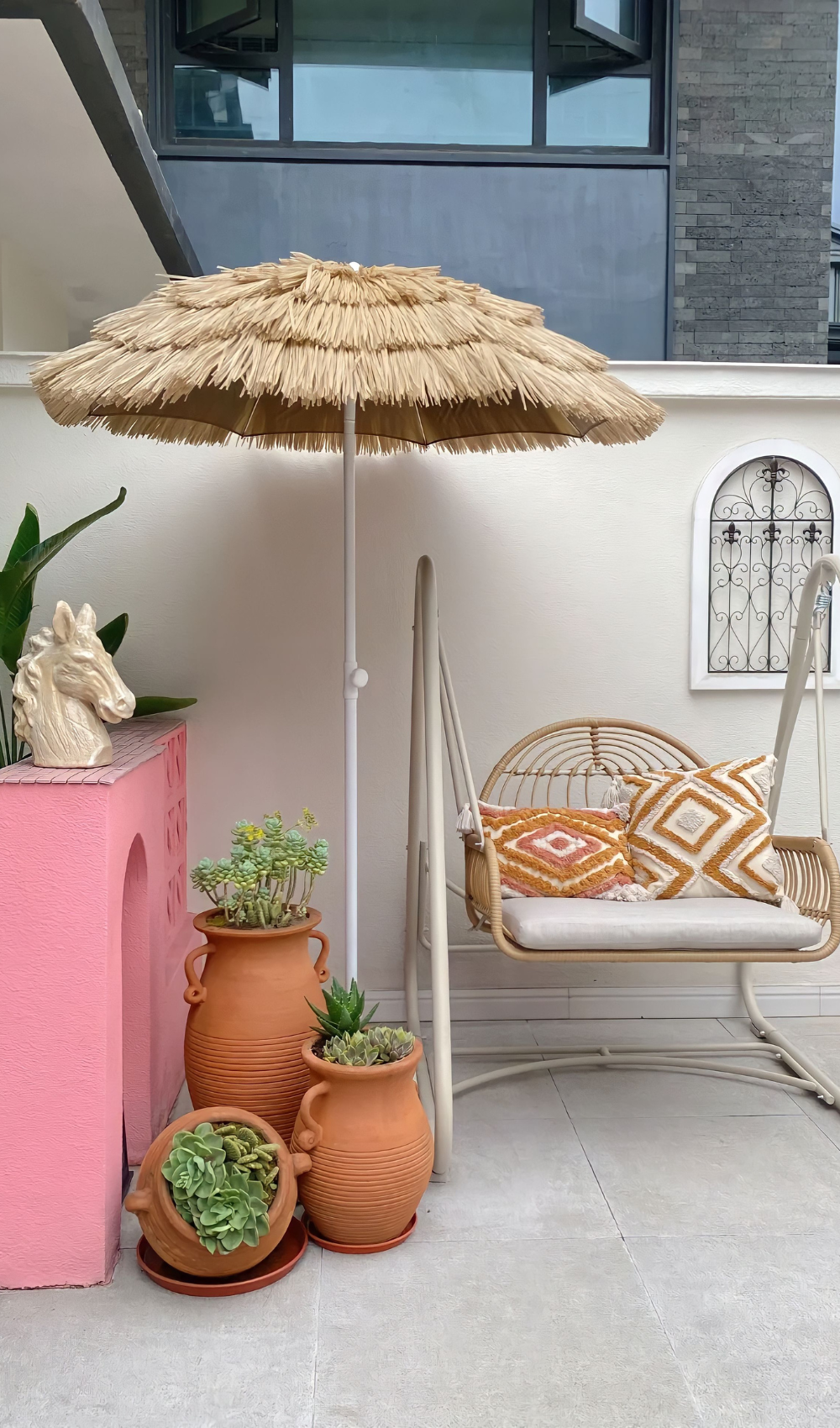 a boho inspired small summer patio with pink orange and white colors, a parasol and an armchair.