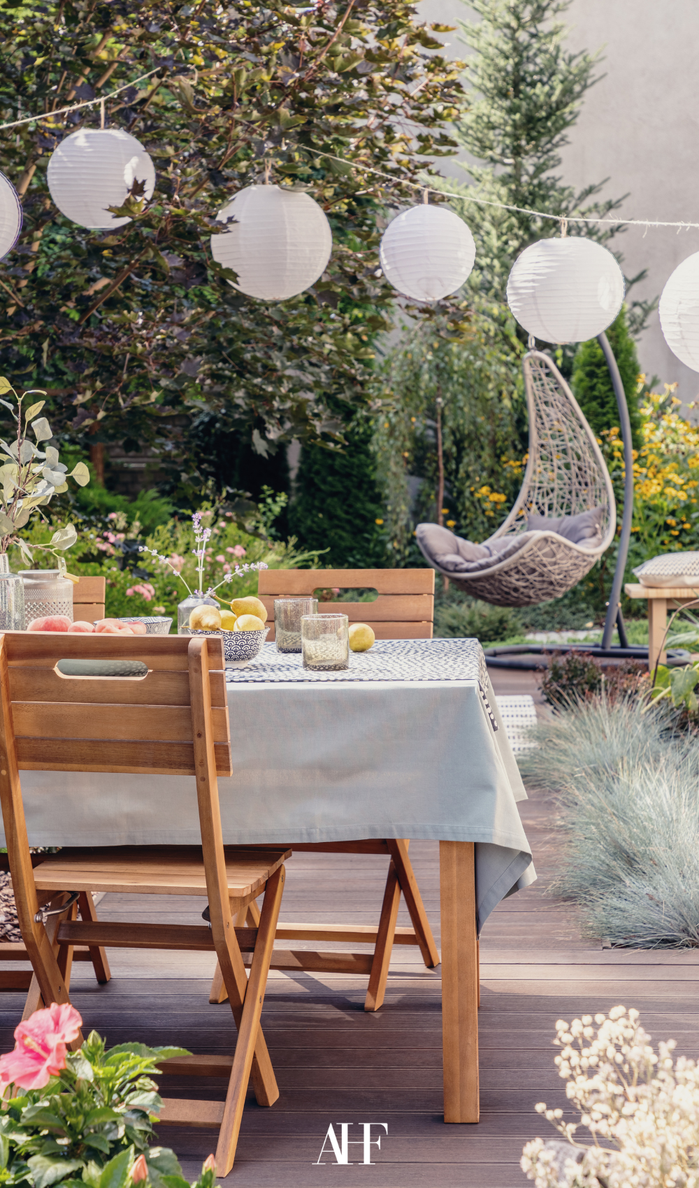 Summer Wind Patio Furniture. A wooden dining table and a wooden chair, a light table cloth and lots of decoration. Cozy lighting and plants.