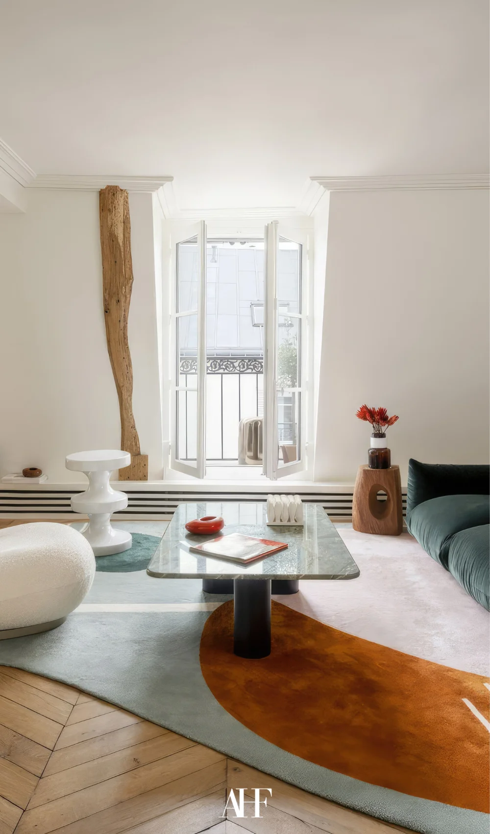 A small apartment living room with one large window, a green sofa and a white armchair. A marble coffee table.