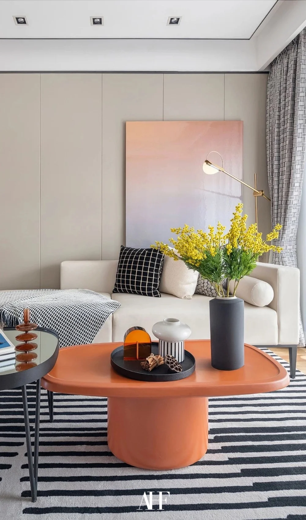 A colorful living room with an orange coffee table, a white sofa and a pastel wall art. A striped rug.