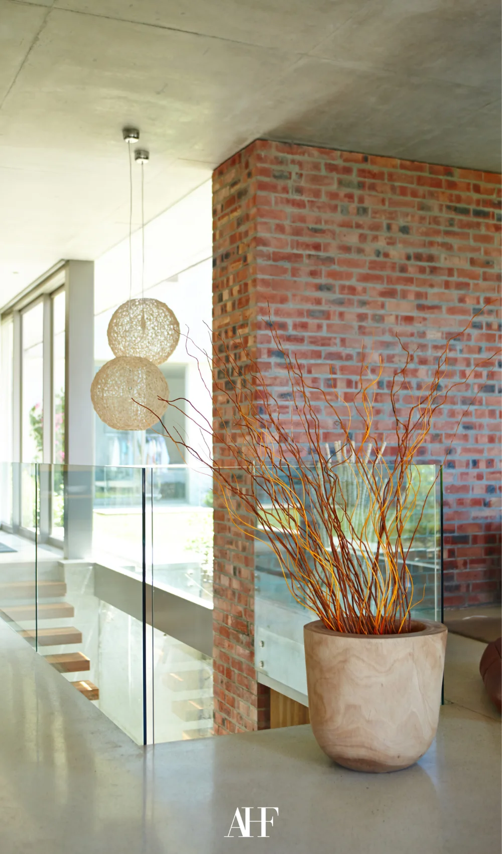 An exposed brick wall with glass railing for the stairs and a large concrete pot with a plant in it.