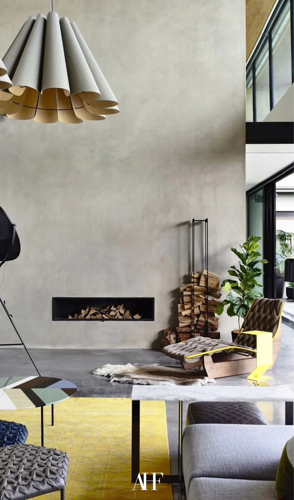 A concrete wall with a fireplace built in. A yellow rug and industrial interior design furniture pieces.
