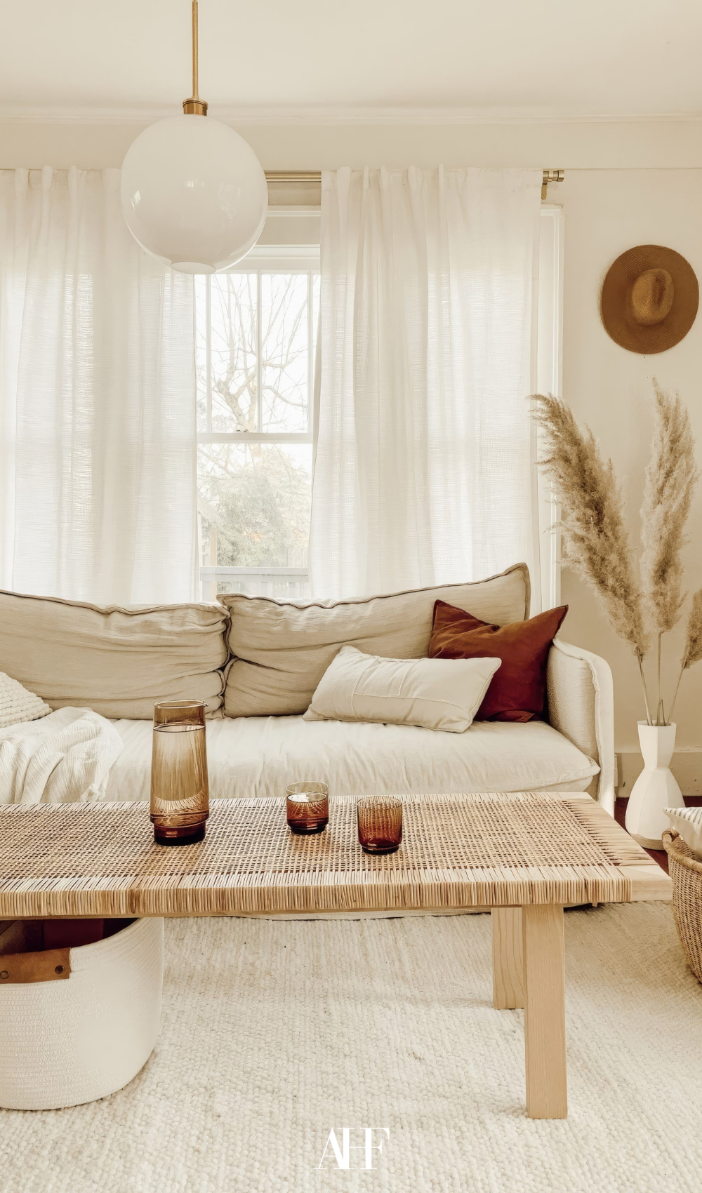 A bright and airy living room with a beige sofa and a rattan chair, large wundows behind the sofa.