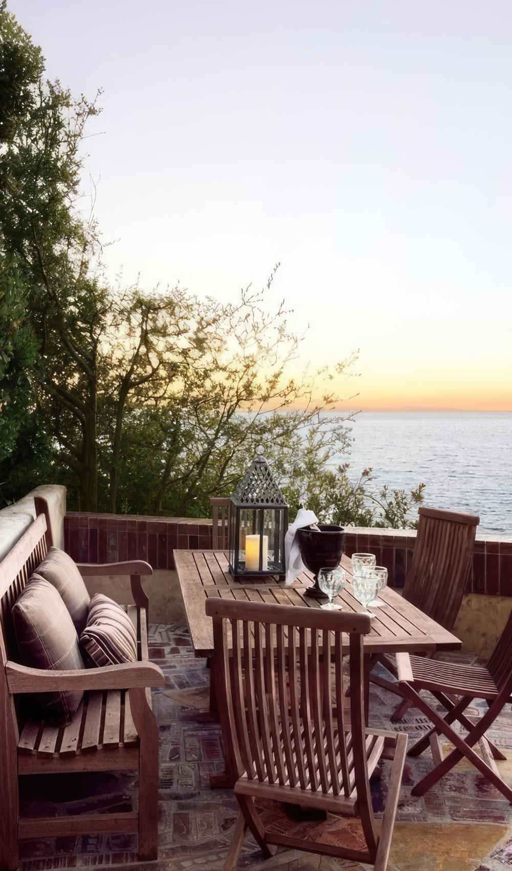 A bautiful view of a small summer patio with wooden furntiure pieces and the ocean in the distance.