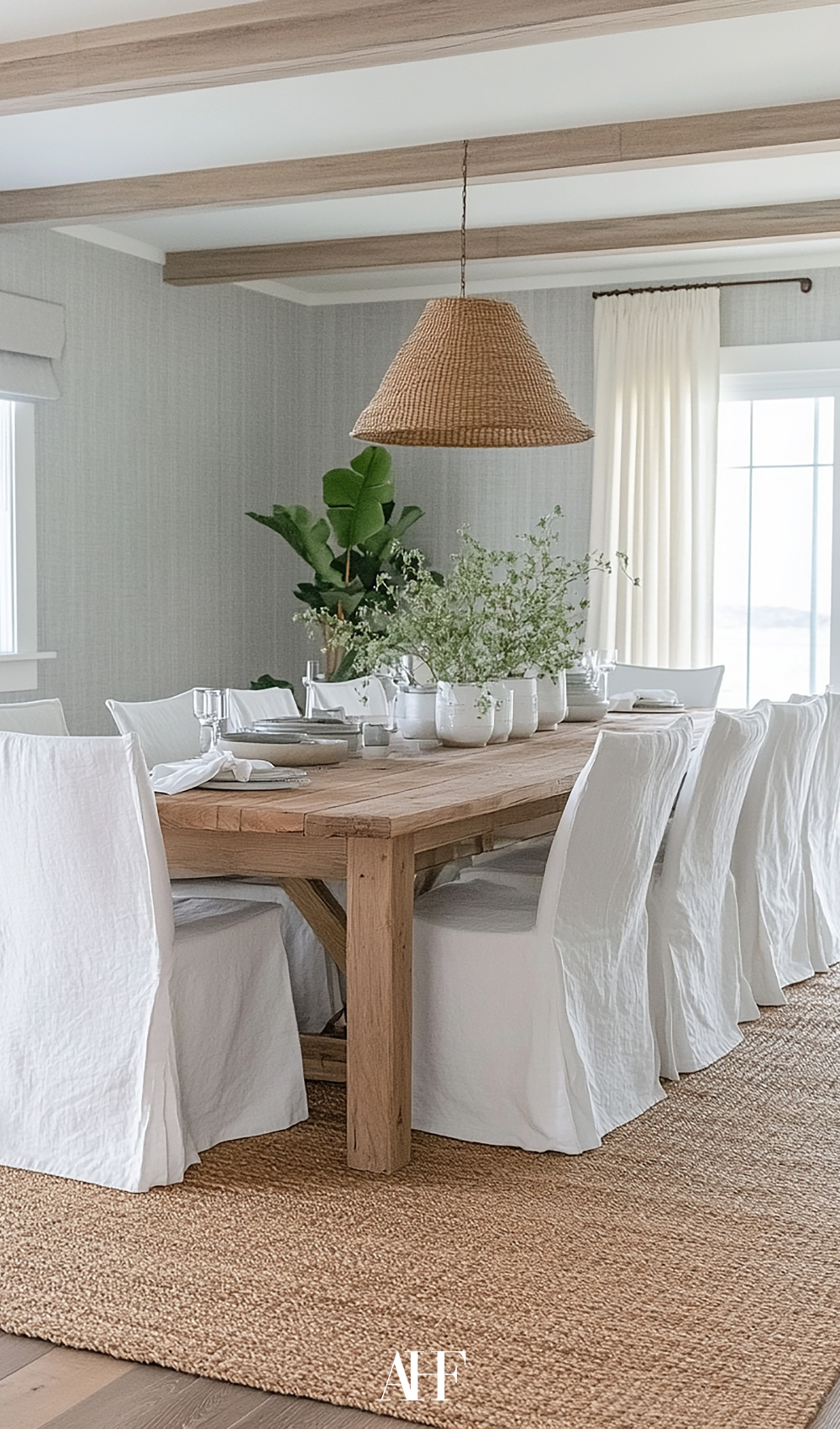 A coastal dining room with a wooden dining table, white chairs and a rattan ceiling lamp. A perfect jute rug. 