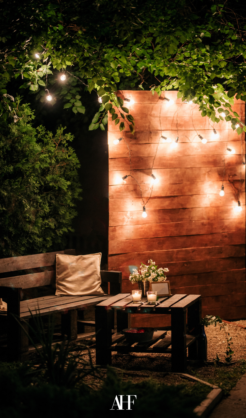 A cozy patio decorated with a wooden bench and a wooden coffee table, cozy string lights. Summer wind furniture.
