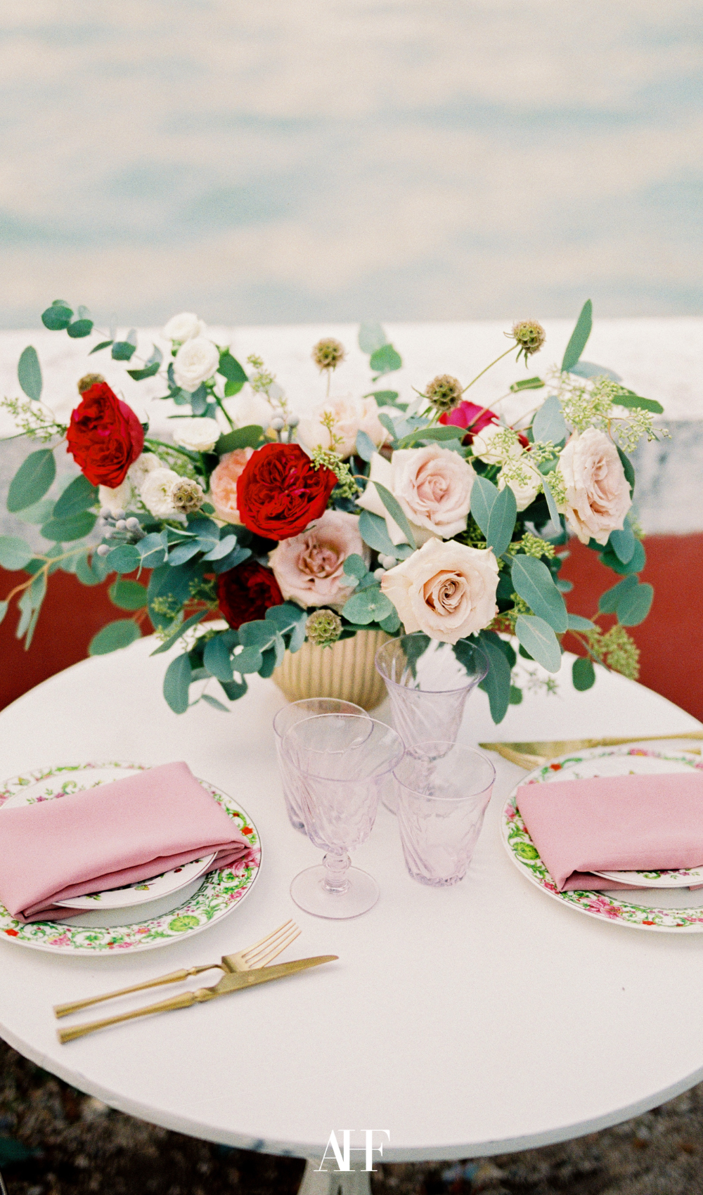 a pink summer table setting, with a light pink tablecloth, pink napkins and a large pink bouquet of flowers as a centerpiece.