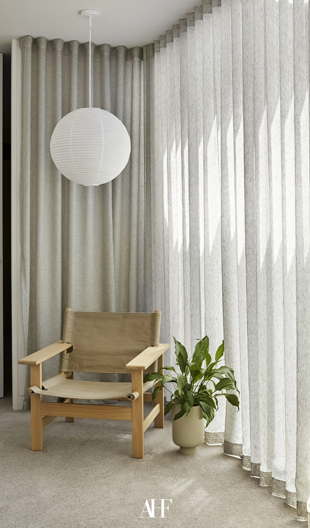 A beautiful corner with a wooden armchair, a plant in a planter and sheer linen curtains on the large windows.