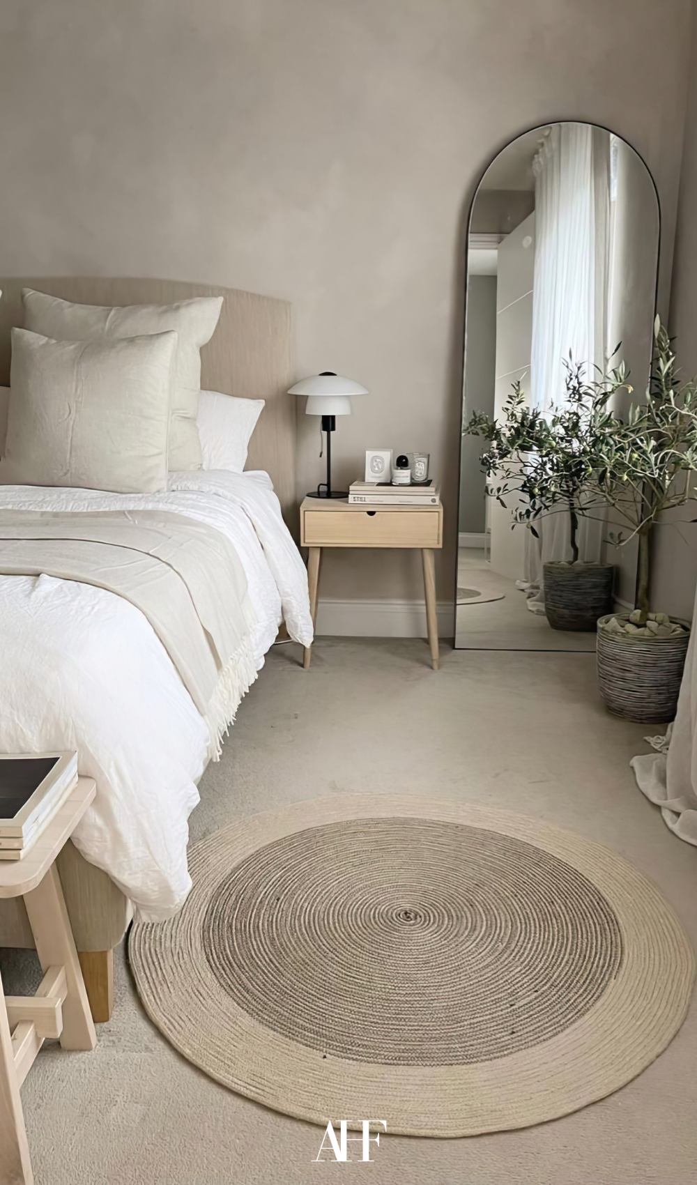 Bedroom with a large bed, a round rug and a mirror against the wall. Beige colors and a perfect rug.