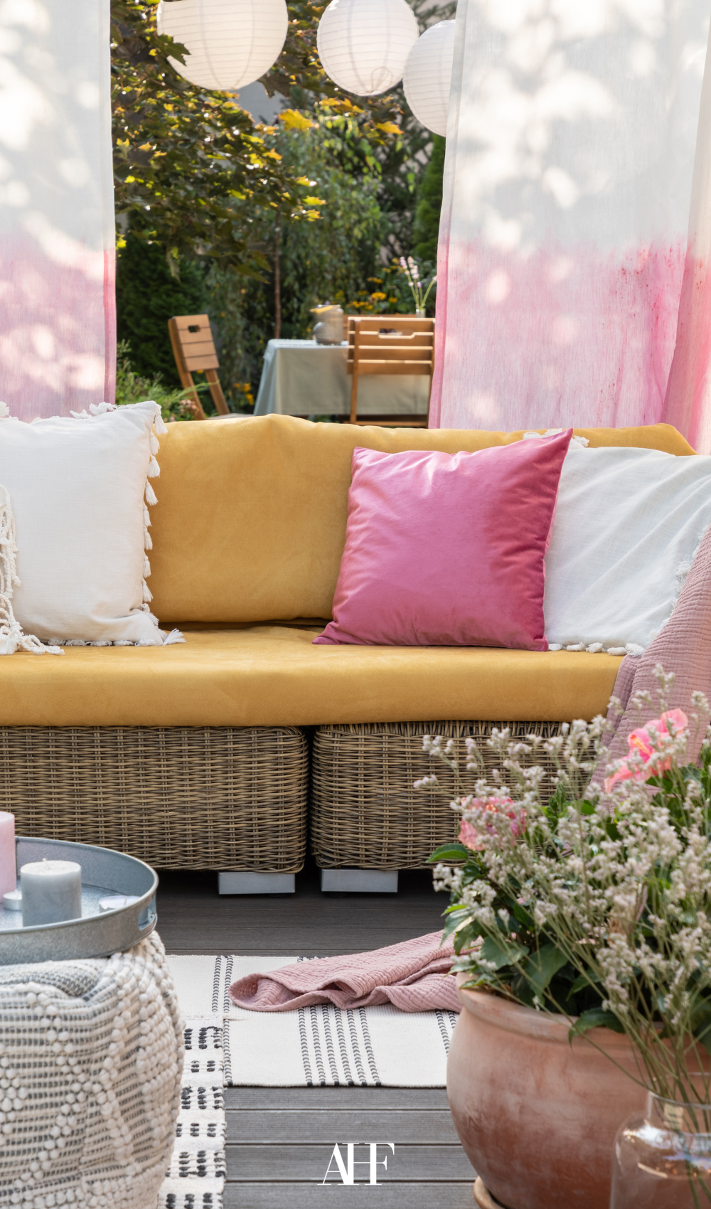 Colorful summer patio with yellow, pink and white pillows. flowers and pink curtains.