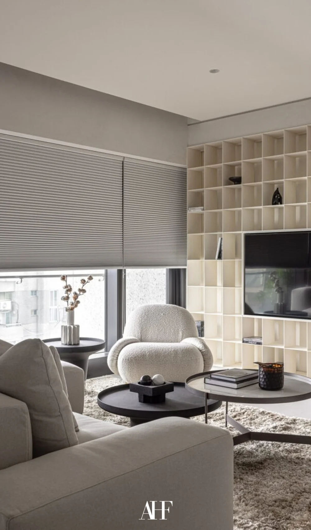 Small apartment living room with a large window, a white sofa, a white armchair and two black round coffee tables. A built in shelf on the TV wall.