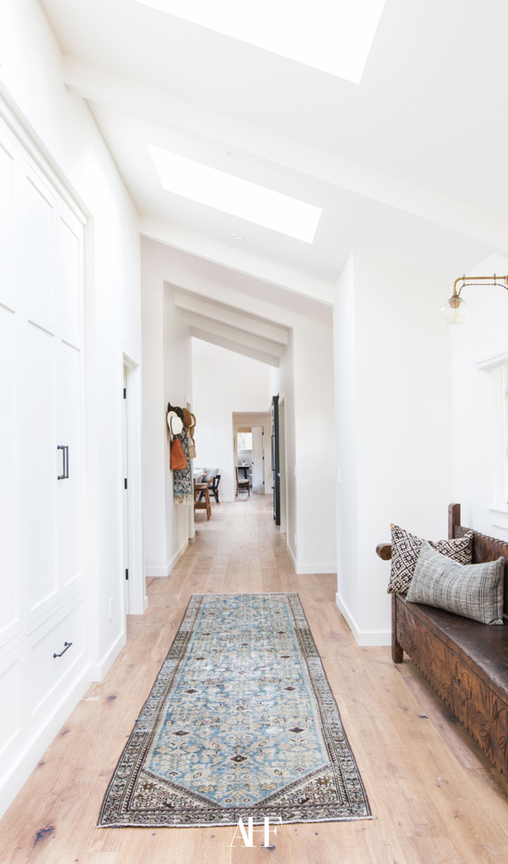 A hallway with a runner rug and a wooden bench. 