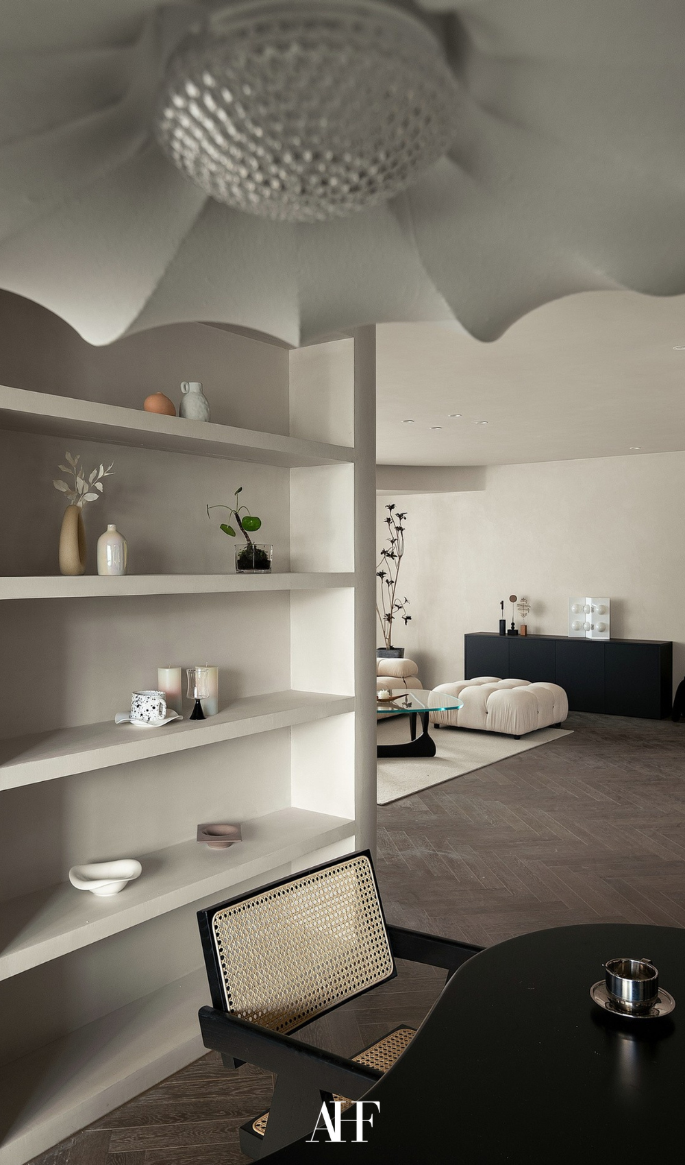 A closeup on a ceiling lamp, a rattan dining chair, a white bookshelf and a living room with a perfect rug in the distant. 