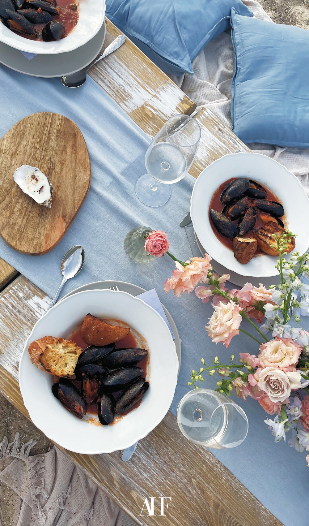 a summer dining table by the beach with a wooden table, blue pillows and a blu tablerunner.
