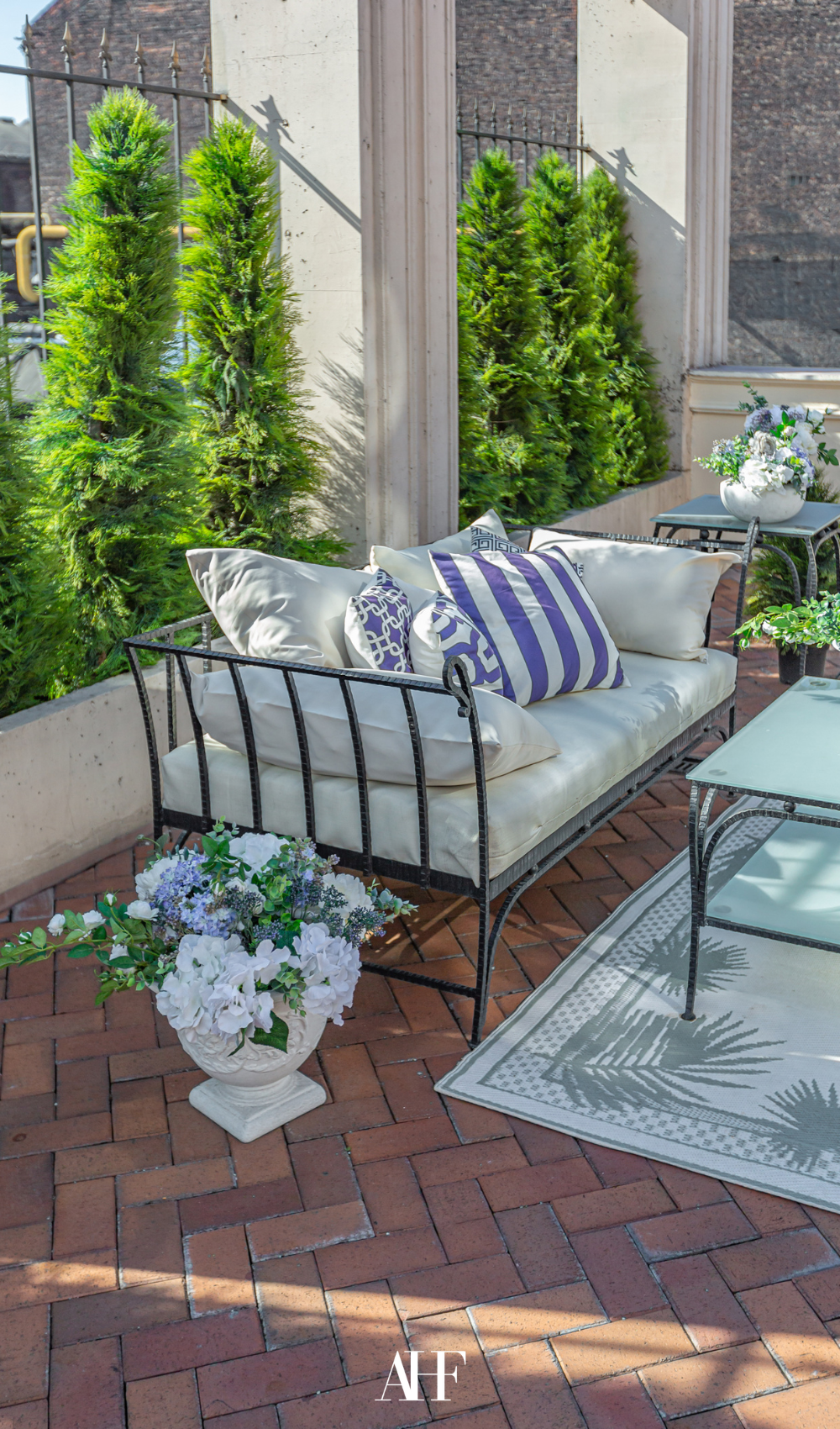 A small summer patio with a black metal couch and white and blue cushions, a white and blue flower.