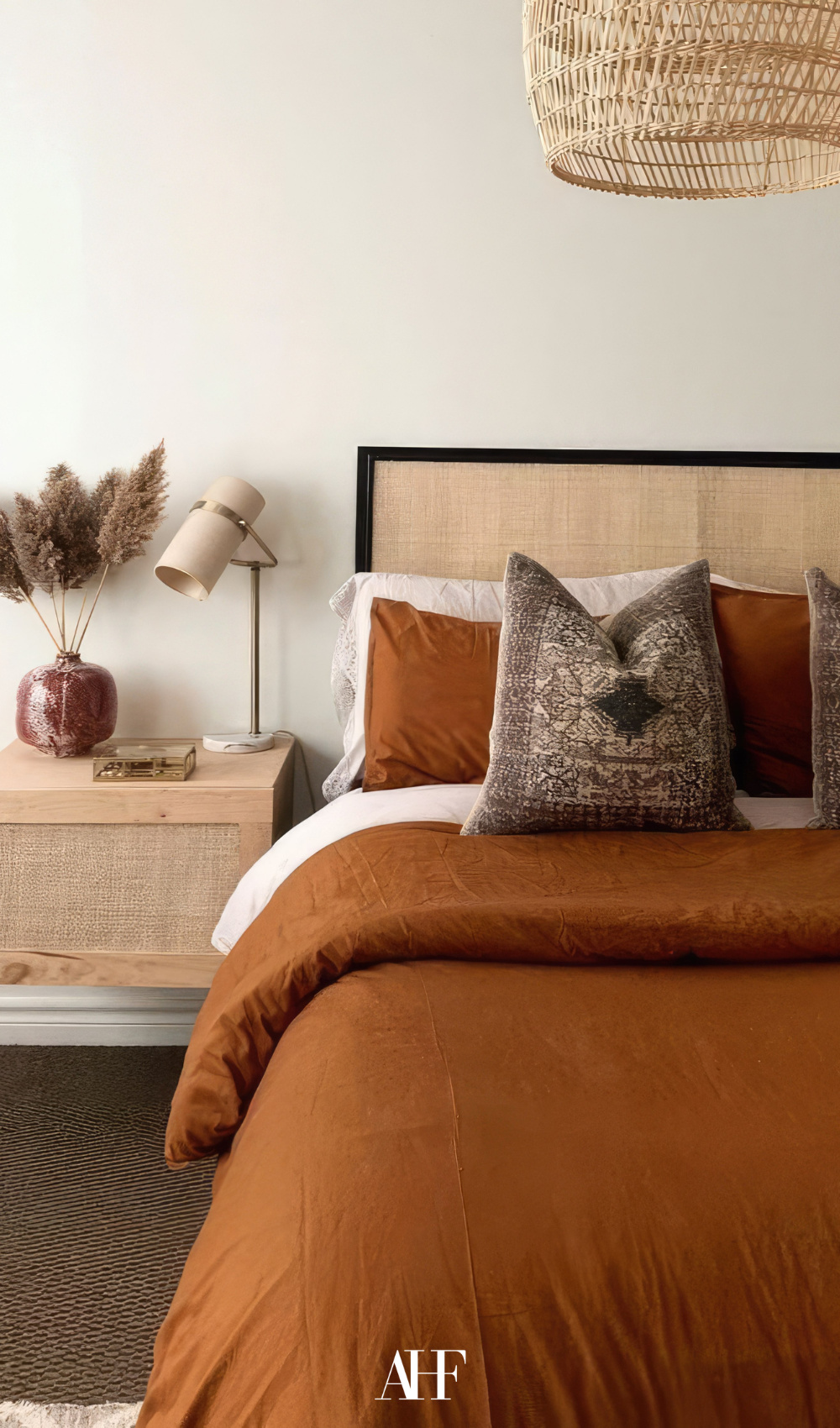 A beautiful eclectic bedroom with rust bedding, a patterned pillow and a wooden bedside table.