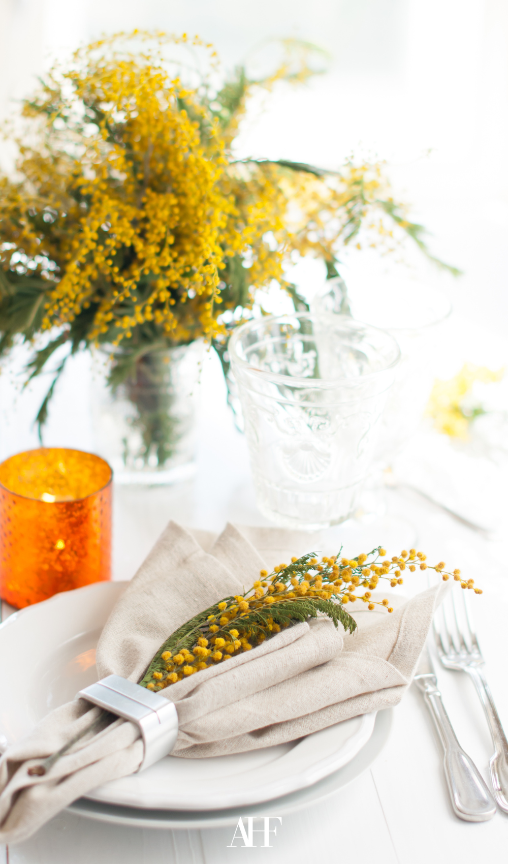 summer table settings with a large yellow flower as a centerpiece, white dinnerware and light outside.