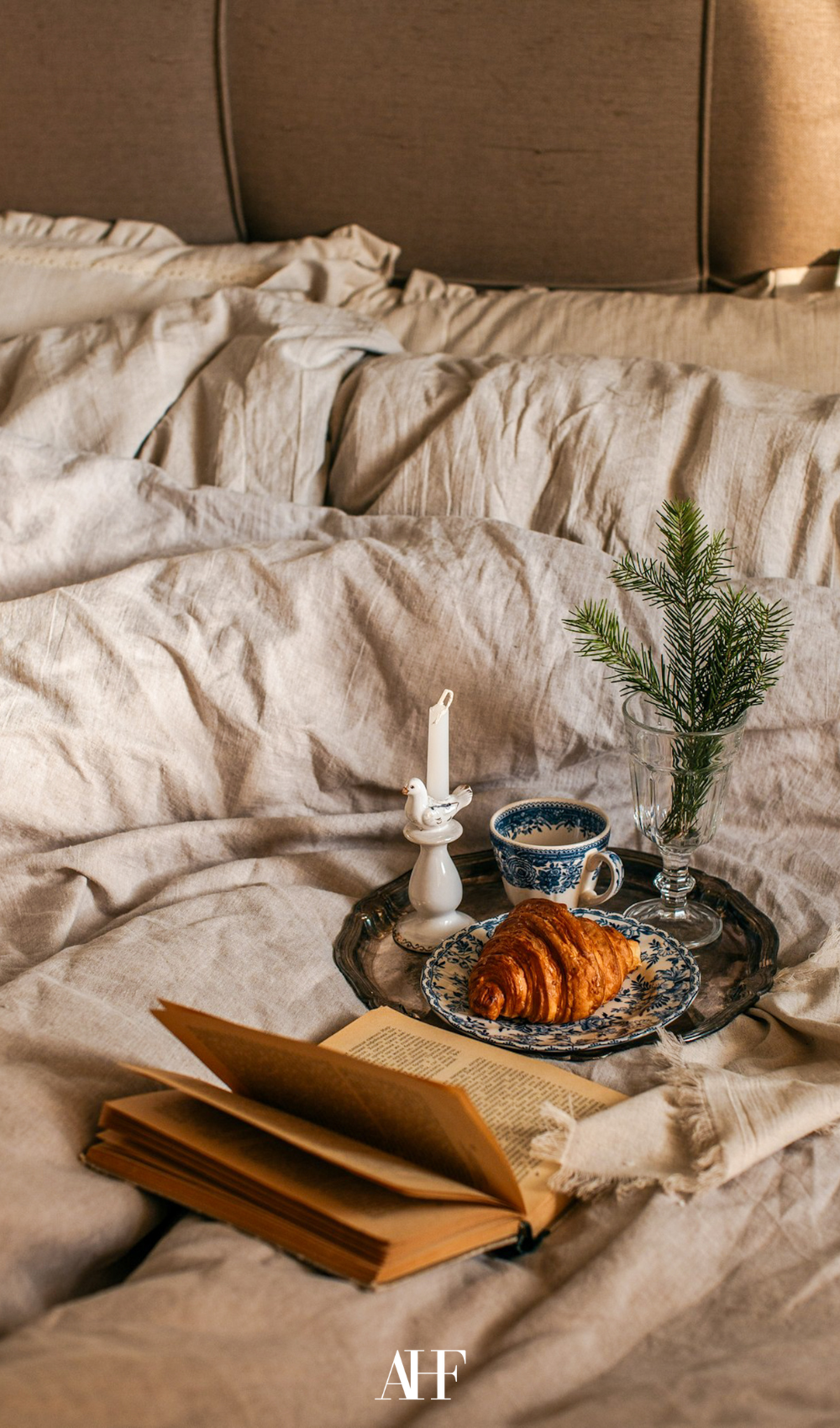 A beige bedding with a brick with breakfast on it and a book.