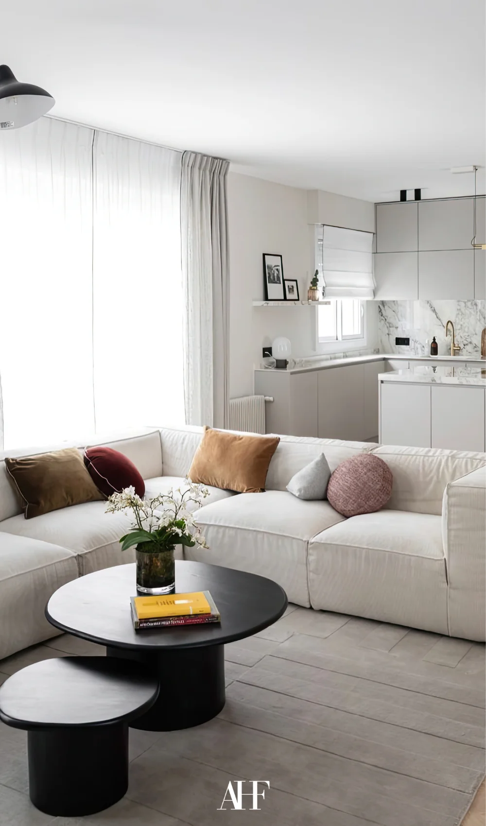 A large white sofa with a black coffee table, a white kitchen in the background. A small apartment living room.