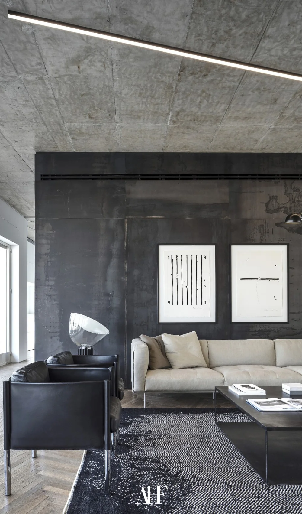 Industrial interior design with black walls, a beige sofa and a black armchair. A black coffee table, white artwork and a grey rug.