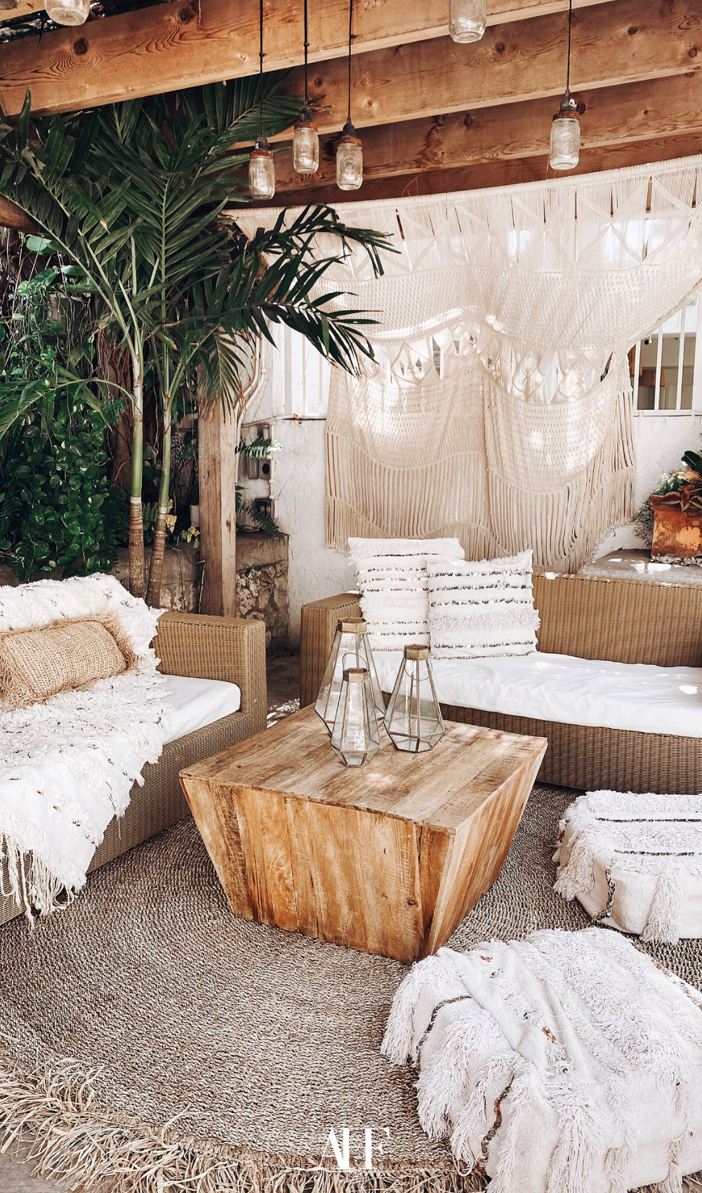 A boho inspired summer patio with a wooden coffee table. Two couches with boho throw pillows and lots of decorations. A palm tree.