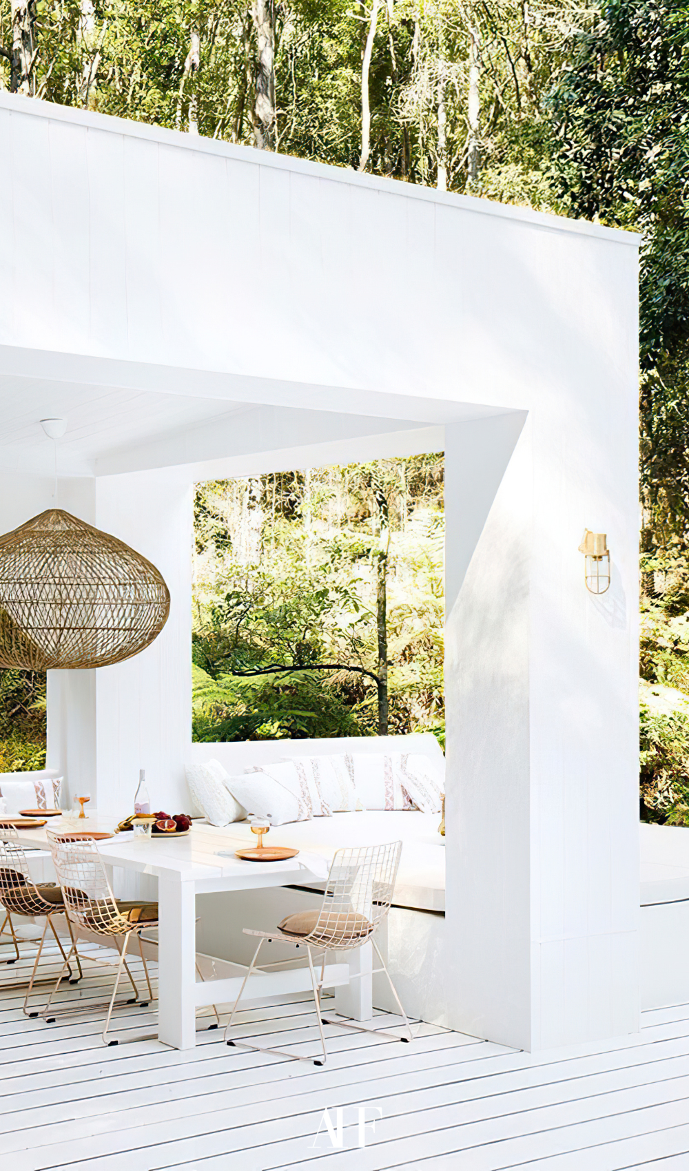 White patio wih a white table and wooden chair, a boho ceiling lamp and a white couch in the backgroound.