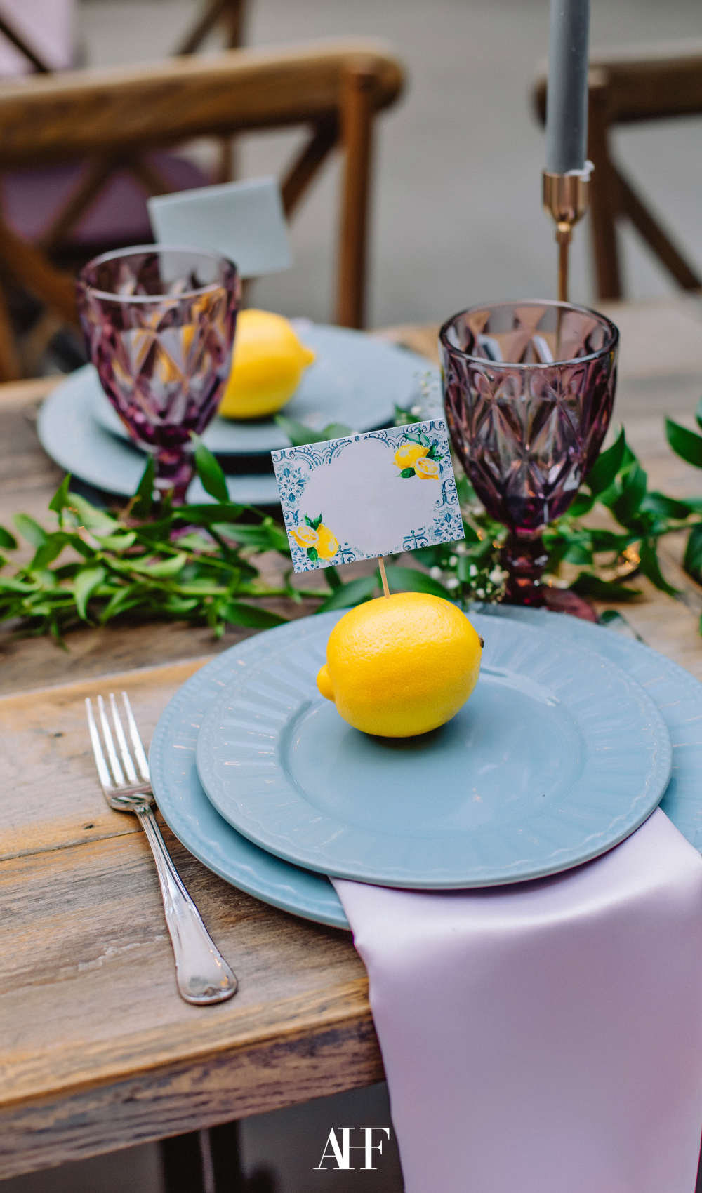 a summer table setting with a blue dinnerware, a citrus with a name card and a wooden table.