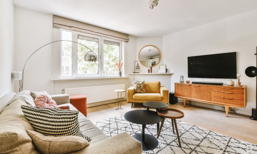 small apartment living room layout ideas with a yellow armchair, a rug, a wooden tv bench and a tv. a large window. storage furniture for small apartments.