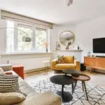 small apartment living room layout ideas with a yellow armchair, a rug, a wooden tv bench and a tv. a large window. storage furniture for small apartments.