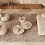 A cozy living room with a beige sofa, two beige armchairs and a seof three coffee tables. A perfect rug to tie the space together and a wooden bench.