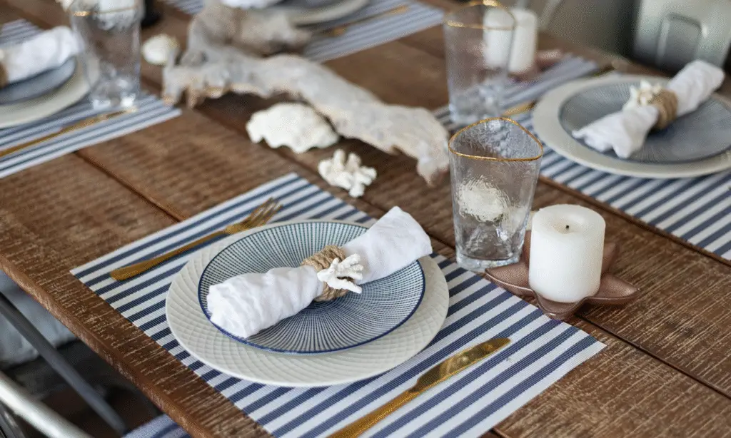 A wooden dining table with blue and white dinnerware and a blue and white striped coaster.